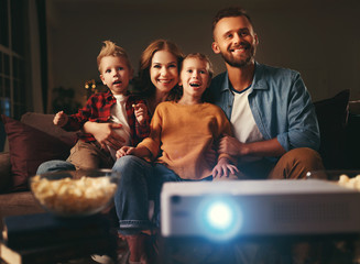 family mother father and children watching projector, TV, movies with popcorn in   evening   at...