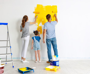 Repair in apartment. Happy family mother, father and child daughter  paints wall .