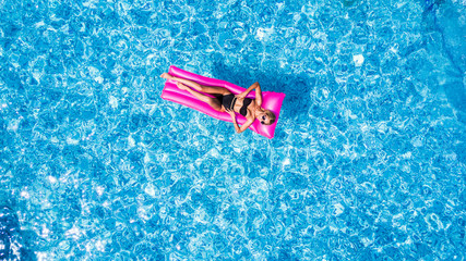 Young woman in a bikini swimsuit floating on an inflatable pink mattress. Top view