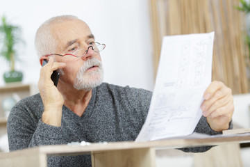 senior man on the phone assembling a furniture