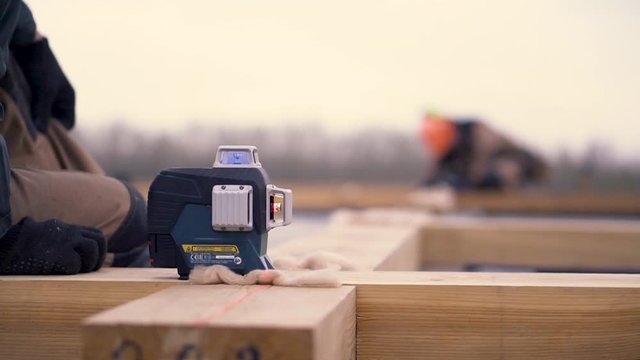 Close up of laser measurement level for construction works standing on a wooden bar at the construction site. Clip. Male builders making framework.