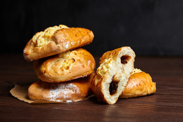 Wheat buns with jam and curd filling on a wooden table, closeup. Bakery, group of buns with cottage cheese stacked on baking paper on dark background