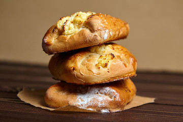 Wheat buns with curd filling on a wooden table, close-up. Bakery, three buns with cottage cheese stacked on baking paper on brown background