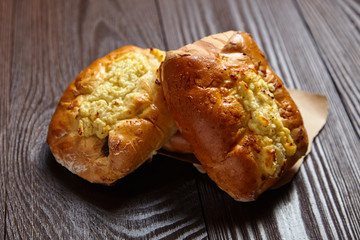 Wheat buns with curd filling on a wooden table, close-up. Bakery, three buns with cottage cheese on baking paper on brown background