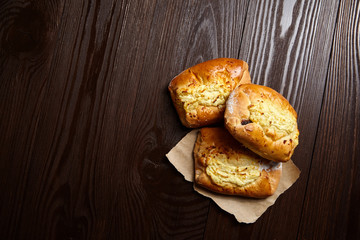 Wheat buns with curd filling on a wooden table, close-up. Bakery, three buns with cottage cheese on baking paper on brown background with copy space, top view