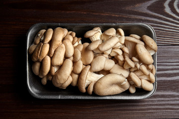 Oyster mushrooms in grey tray on wooden background, top view. Uncooked edible mushrooms on brown table, close-up