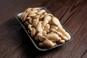 Oyster mushrooms in grey tray on wooden background. Uncooked edible mushrooms on brown table, close-up