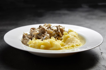 Mashed potatoes with fried oyster mushrooms in a white ceramic plate on a black stone table
