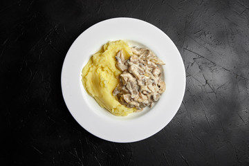 Mashed potatoes with fried oyster mushrooms in a white ceramic plate on a black stone table, dark background, top view