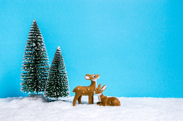 Winter theme with miniature reindeers and Christmas trees on blue background with copy-space