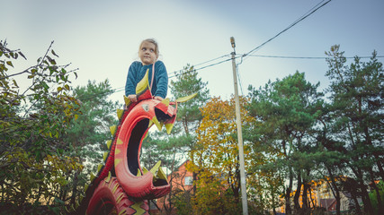 A charming little girl in casual clothes sits on a structure of the colored tires in a countryside.