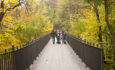 family walks on a foot bridge in the park in autumn