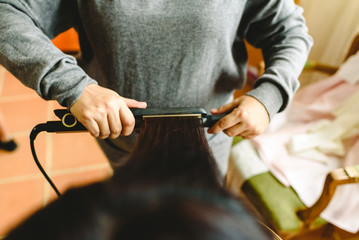 Hairdresser smoothing a woman's hair with a hair straightener.