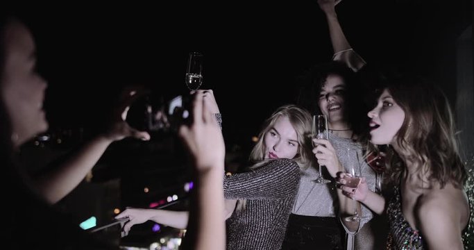 Female Friends partying on urban rooftop and taking picture with smart phone