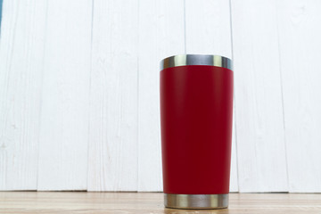 Red colour stainless steel tumbler or cold and hot storage cup on wood.