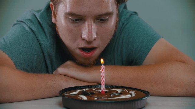 A man is blowing out a candle on a birthday cake