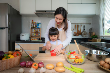 Portrait of beautiful Asian young woman and her daughter cooking salad for lunch and cutting red...