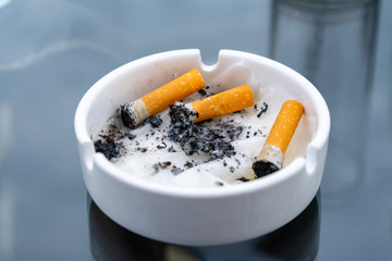 White dirty ashtray with cigarette stubs. Cigarette.