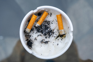 White dirty ashtray with cigarette stubs. Cigarette.