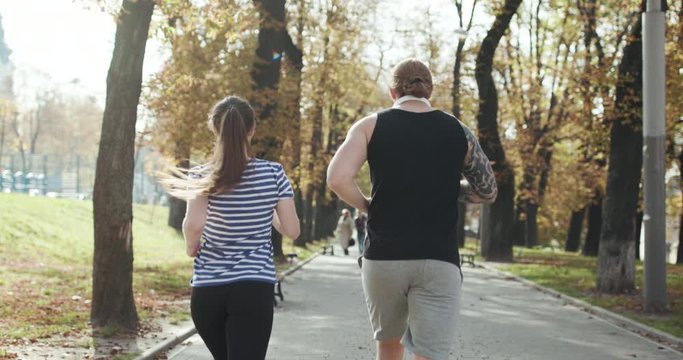 Young guy and girl working out. Fitness couple running together on sunny park. Man and woman at sport training together. Athletic newlyweds exercising together. Sport couple run together in park.