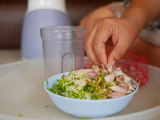 A woman's hand preparing / putting food ingredients in a small bowl for blending for cooking food at home
