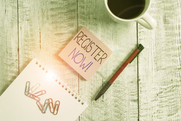 Text sign showing Register Now. Business photo showcasing official list or record showing or things into forum Stationary placed next to a cup of black coffee above the wooden table