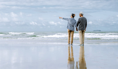 Naklejka premium Asian senior couple or elderly people walking and siting at the beach on their weekend vacation holiday. Retirement vaction concept.