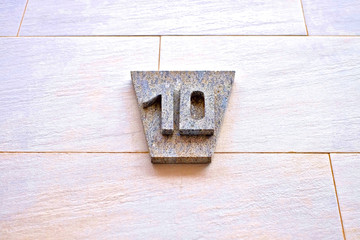 Number 10, ten, gray plate on a light brown wall surface.