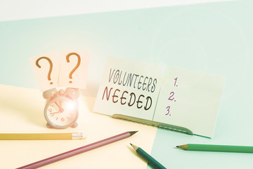 Writing note showing Volunteers Needed. Business concept for need work or help for organization without being paid Mini size alarm clock beside stationary on pastel backdrop