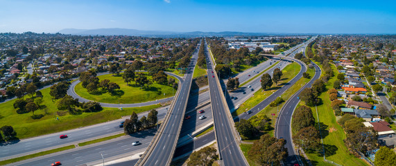 Naklejka premium Straight road passing through interchange and leading to mountains in the distance. Aerial view in Melbourne, Australia