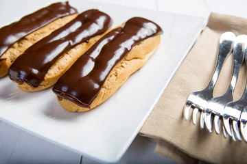 Chocolate eclair, filled with fresh whipped cream and topped with chocolate icing on a white plate