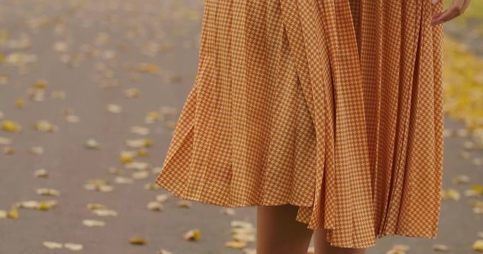 Close-up of a mustard dress with crows feet print falling down. Camera following the dress down to Caucasian female legs in autumn boots. Cinema 4k footage ProRes HQ.