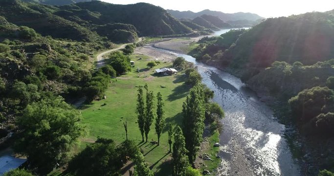 Aerial panoramic view traveling along clean river valley towards lake at wild forest landscape at sunset. Volume light. Rio grande, Nogoli, San Luis, Argentina