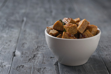 White deep bowl with fried pieces of tofu cheese on a wooden table.