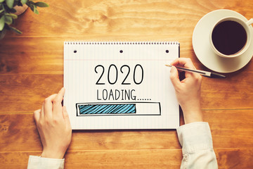 Loading new year 2020 with a person holding a pen on a wooden desk