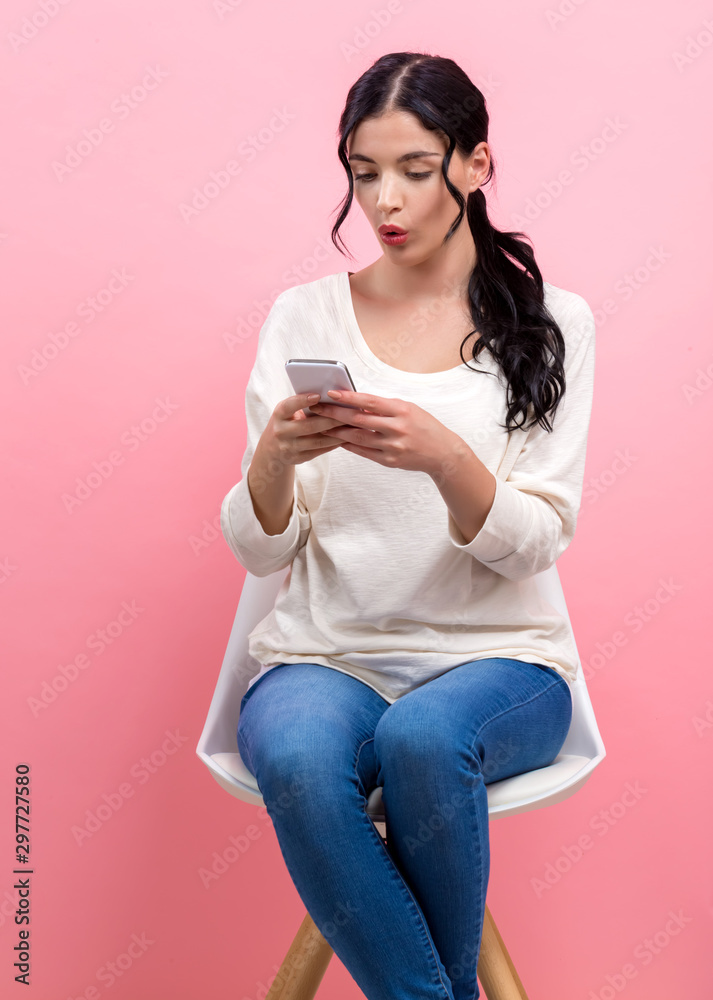 Wall mural young woman staring at her cellphone on a pink background