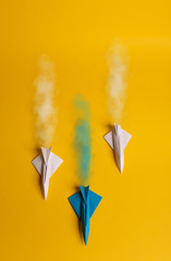 Group of paper plane in one direction and with one individual pointing in the different way on yellow background. Smoke coming out from aircraft tails.