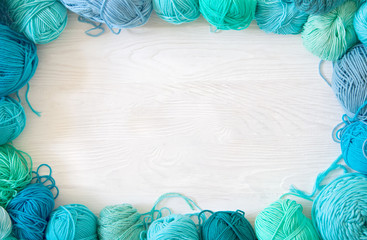 Yarn of green, turquoise, aquamarine and blue colors. White wood background. Knitting needles and...