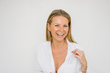 Portrait of happy blonde forty year woman with long hair in white shirt on white wall background...