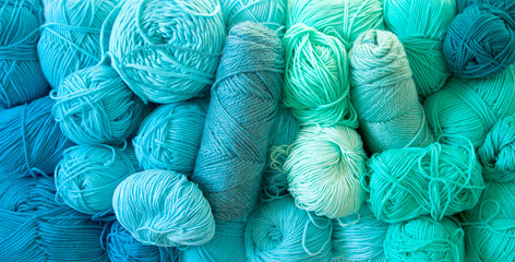 Yarn of green, turquoise, aquamarine and blue colors. White wood background. Knitting needles and...