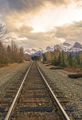 Fototapeta premium Canadian Pacific Railway Line and Distant Mountain Peaks Landscape against Dramatic Stormy Sky Clouds near Canmore, Alberta Foothills of Rocky Mountains