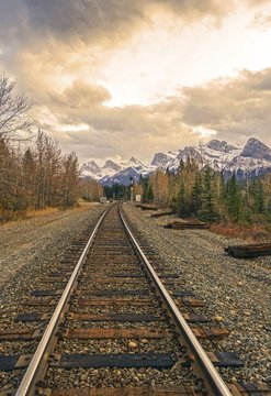 Canadian Pacific Railway Line and Distant Mountain Peaks Landscape against Dramatic Stormy Sky Clouds near Canmore, Alberta Foothills of Rocky Mountains