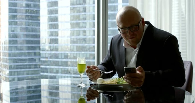 alone businessman is eating salad in daytime in restaurant, reading e-mail in smartphone
