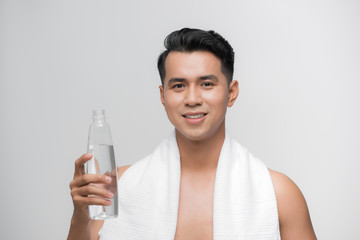 image of handsome smiling man with white towel on his shoulders holding bottle of water after workout white background
