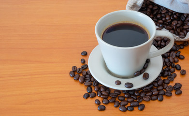 A cup of coffee with coffee beans on the wooden table
