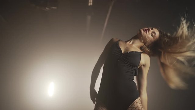 Young woman in black bodysuit with net pantyhose moves plasticly to music in dark room.Concept of sexual dancing,choreography,art.