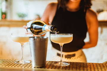 Bartender adding champagne on top of a cocktail in a beautiful glass. Selective focus lifestyle photo with film grain effect