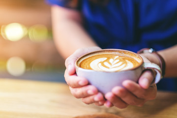 Closeup image of a woman holding a cup of hot latte coffee on wooden table