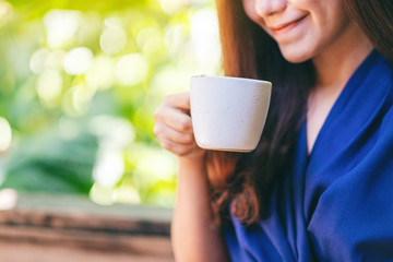 Closeup image of a beautiful asian woman holding and drinking hot coffee in the garden