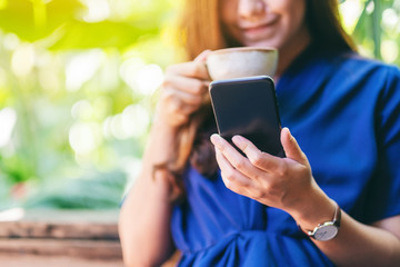 Closeup image of a beautiful asian woman holding and using mobile phone while drinking coffee in the garden
